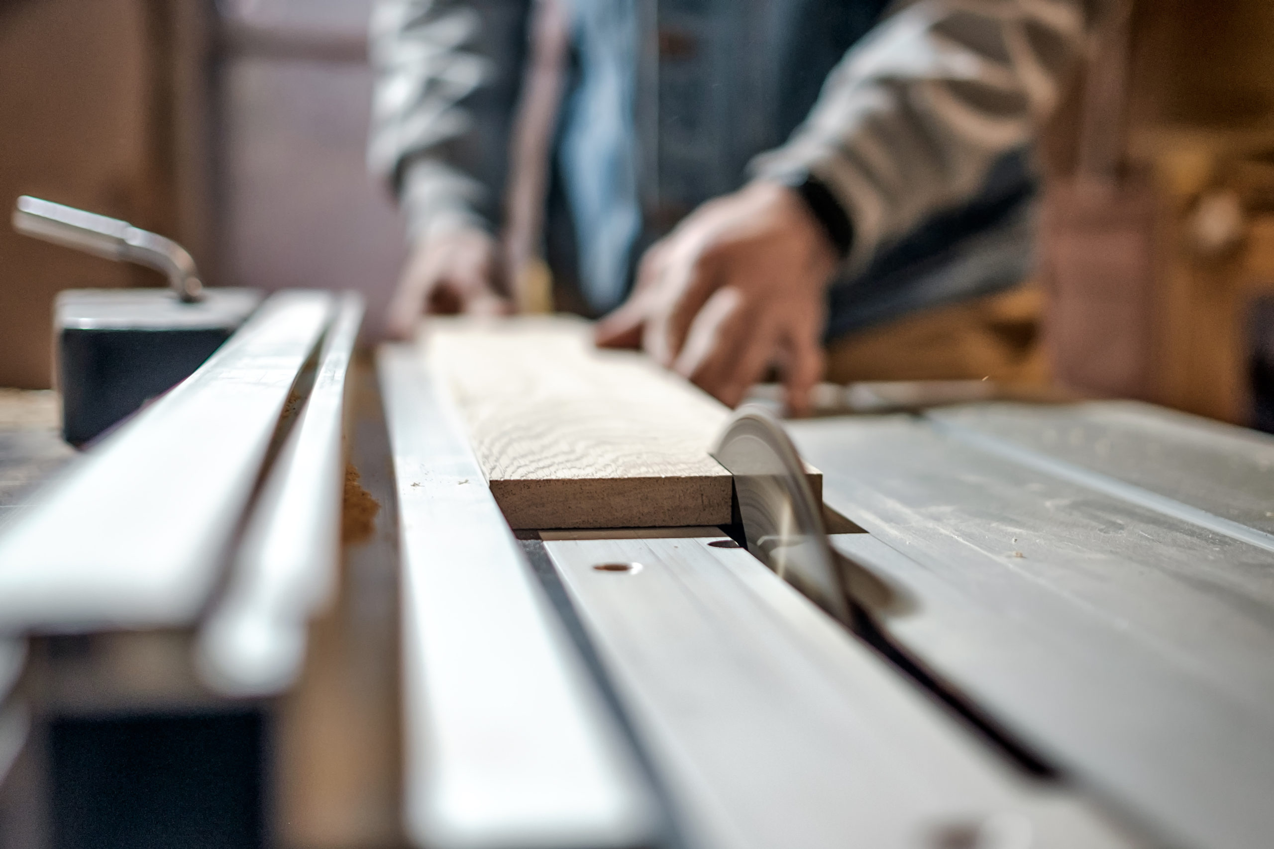 Caucasian man making wooden parts for custom furniture on machine tool called thickness planer in carpentry. Producing lumber concept